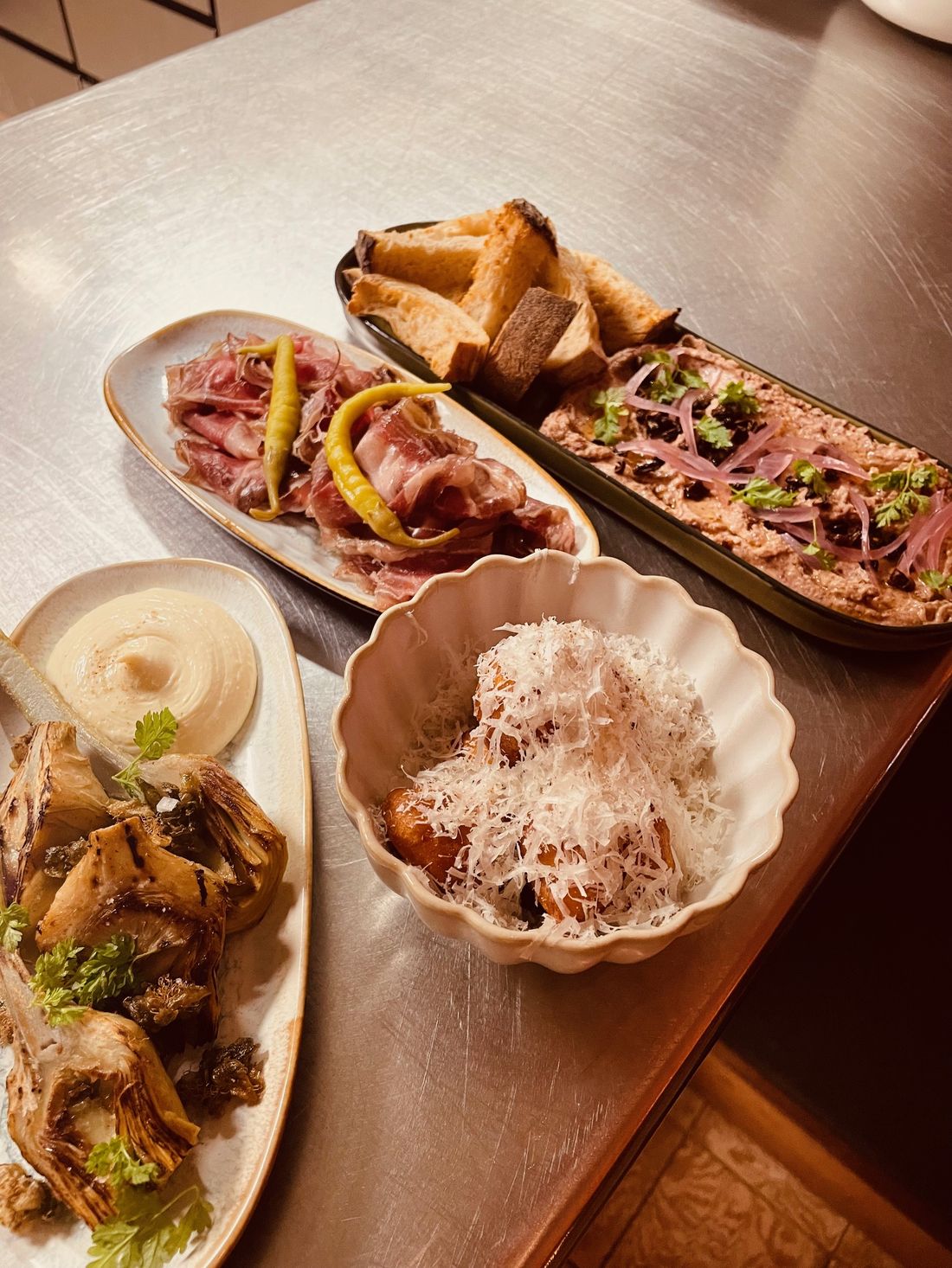 Plusieurs assiettes à partager : charcuteries, houmous, tartinade, artichauts et pain grillé